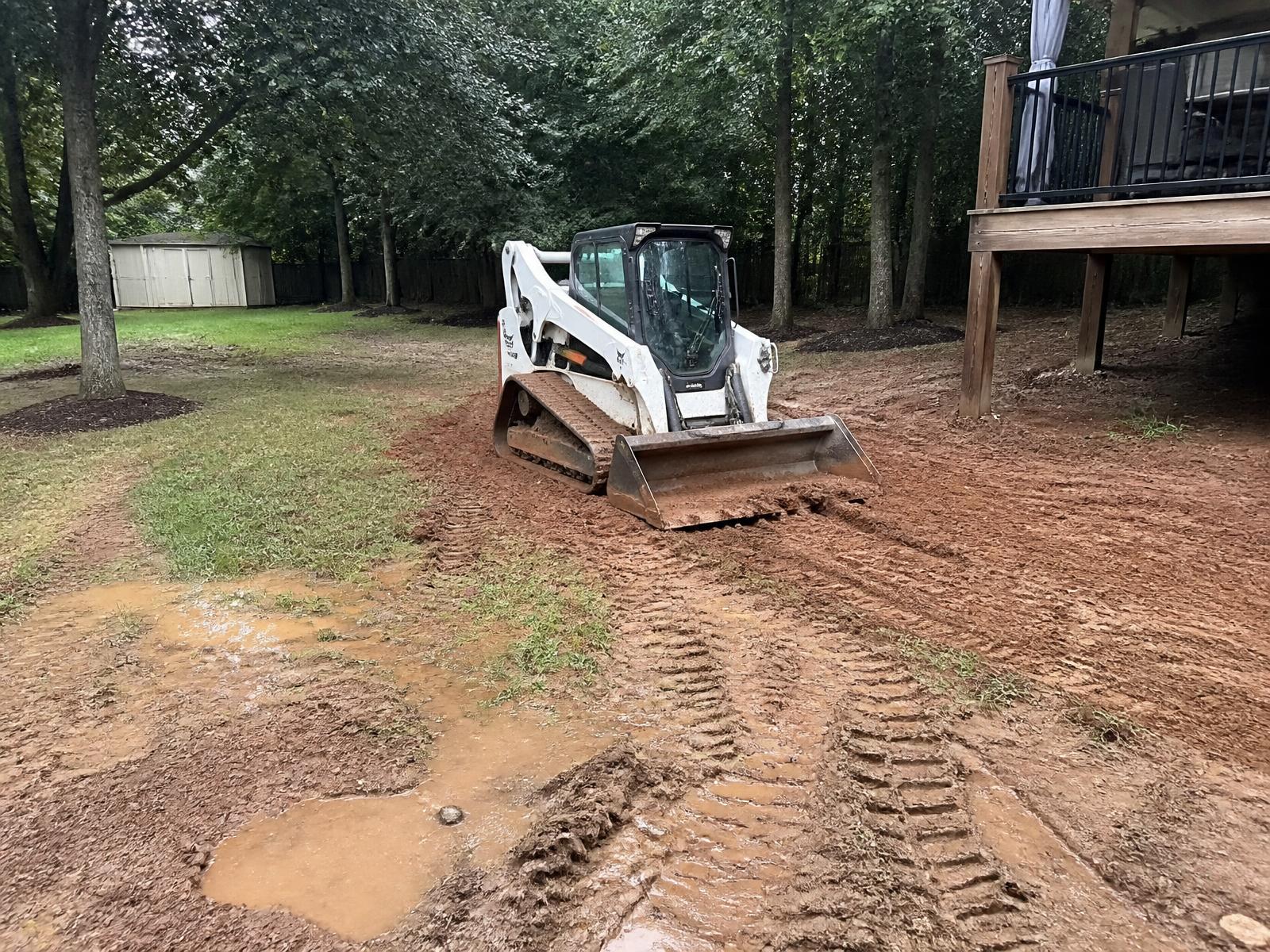 Compact track loader regrading a wet low area of a backyard to slope water away from the deck