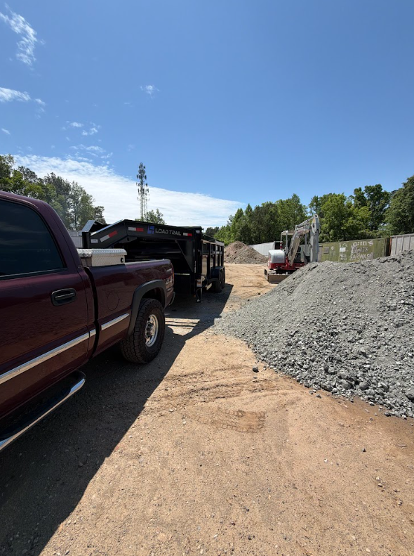 Truck and dump trailer parked beside a large gravel stockpile with a compact excavator loading material