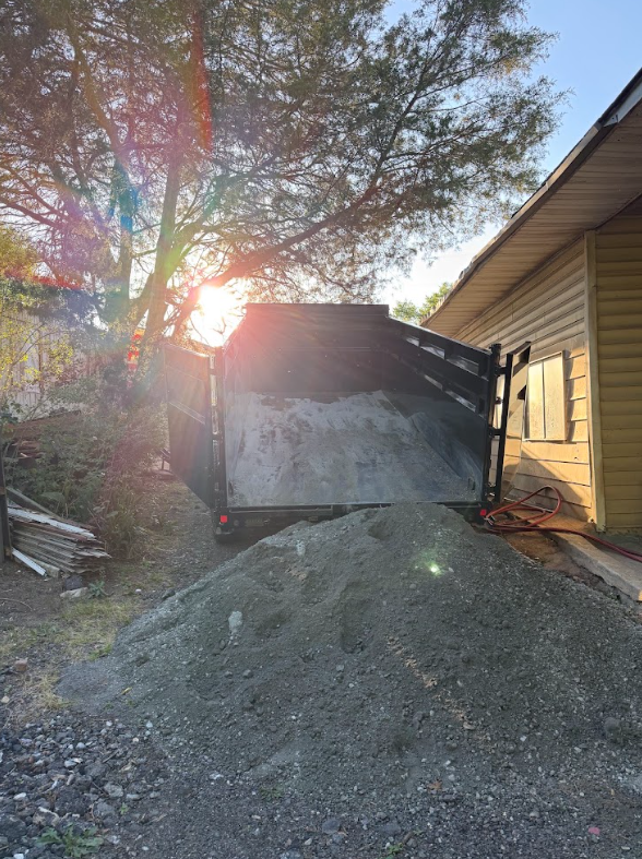 Dump trailer tipping a load of gravel beside a house in late afternoon sun