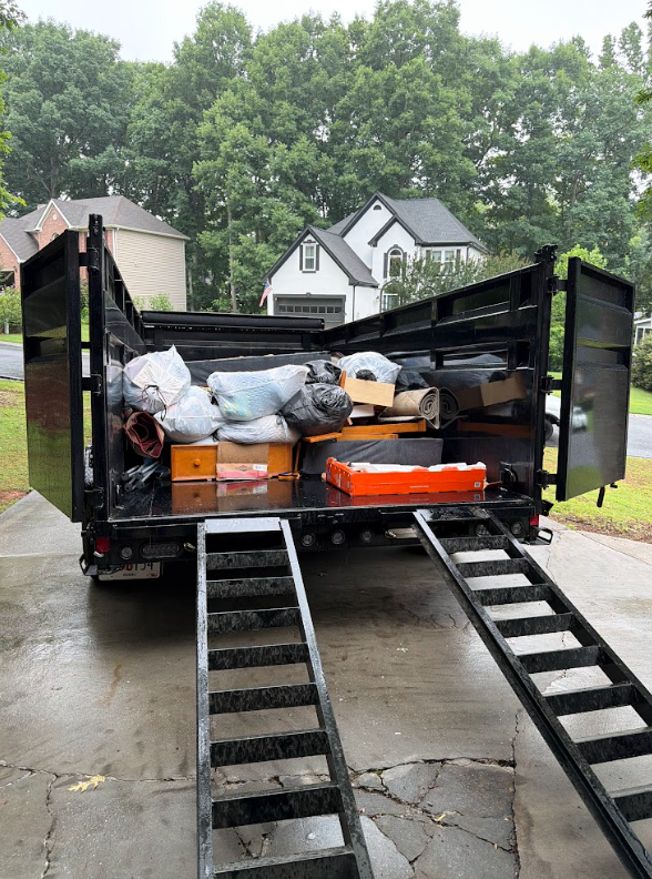 Dump trailer loaded with furniture and household debris on a residential driveway with ramps down