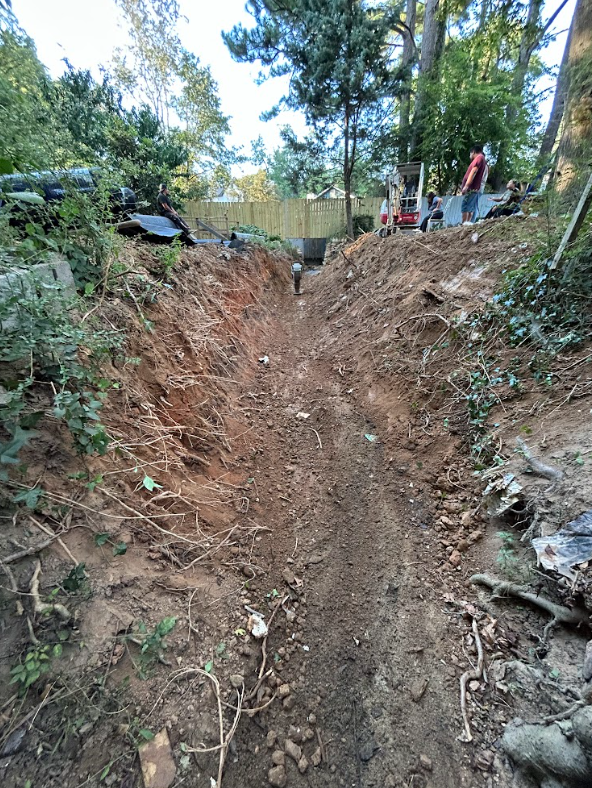 Long open excavation cut between properties with clean trench walls and machine access at the far end