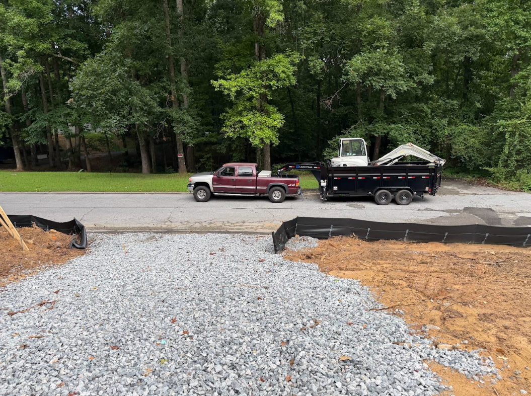 Gravel construction entrance and prepared pad area with a truck and dump trailer parked at the street