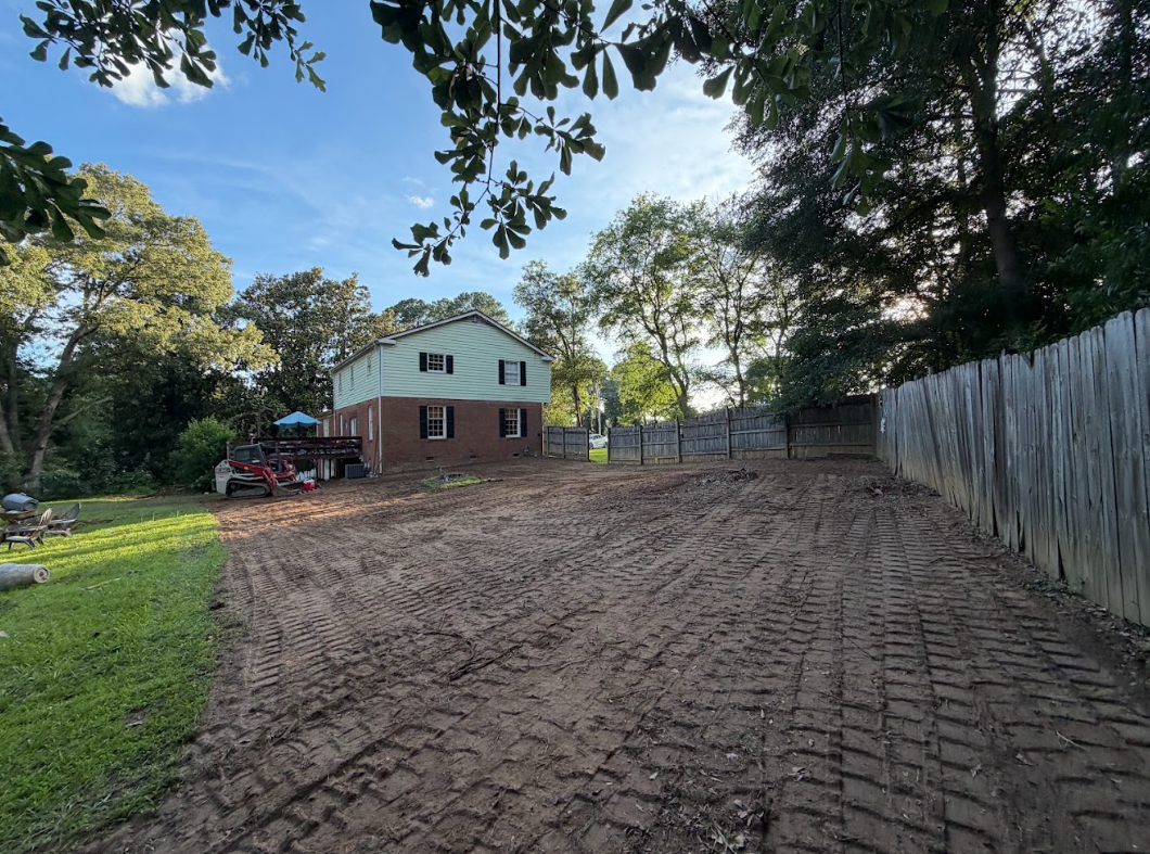 Long side yard graded smooth along a wooden fence line with fresh track marks in the soil
